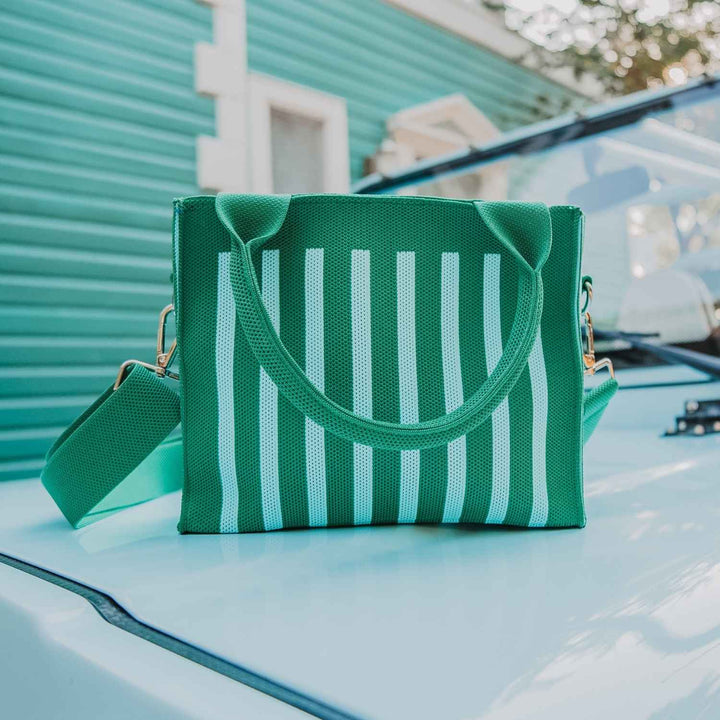 Green and mint stripe mesh mini tote bag with padded top handles and detachable green crossbody strap, sitting on the hood of a light blue vintage car.