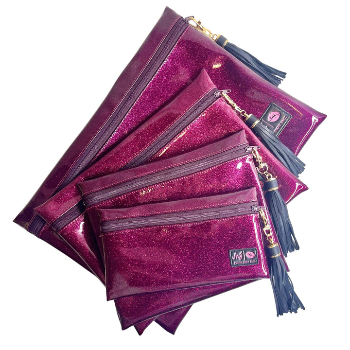 Makeup Junkie Bags magenta hot pink glitter zip makeup bags in four sizes fanned out with navy tassel zipper pulls and branded patches, front view on white background
