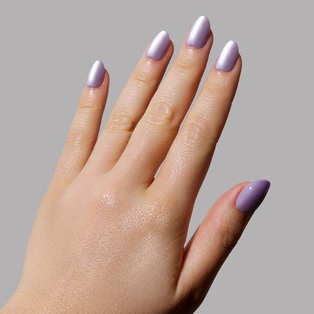 Close-up of hand wearing Glamnetic Mermaid's Tail Press-On Nails in short oval shape with iridescent lavender chrome finish on a gray background