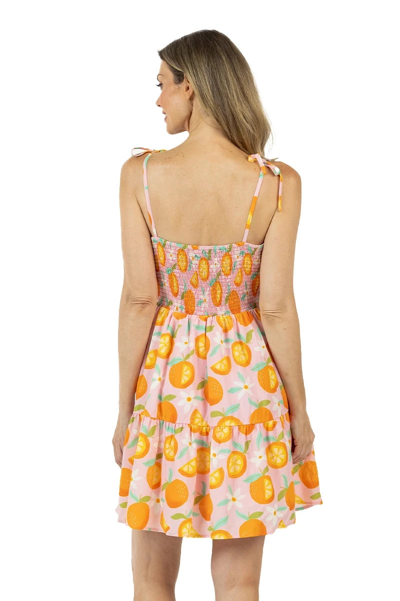 Back view of woman in a pink orange print tiered mini dress showing the smocked back bodice, tie shoulder straps, and two-tier skirt.