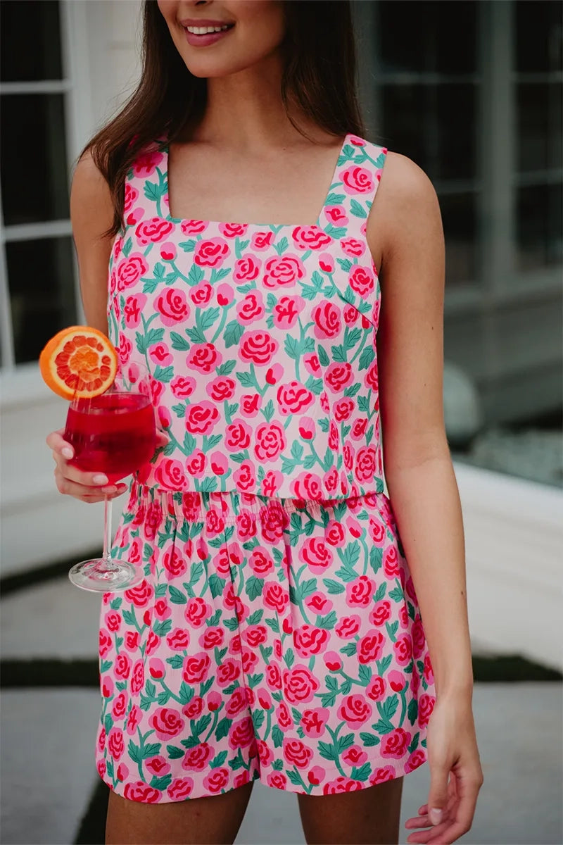 Close-up of woman holding a red cocktail with an orange slice, wearing a pink rose print square-neck crop top and matching elastic-waist shorts.