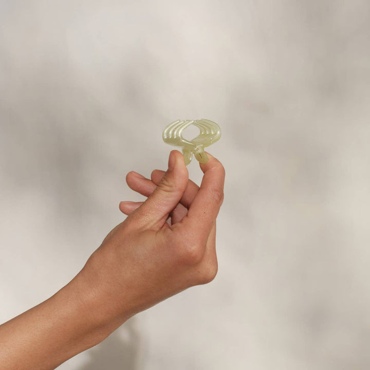 Hand holding a single butter yellow mini cloud claw clip between two fingers against a neutral background.