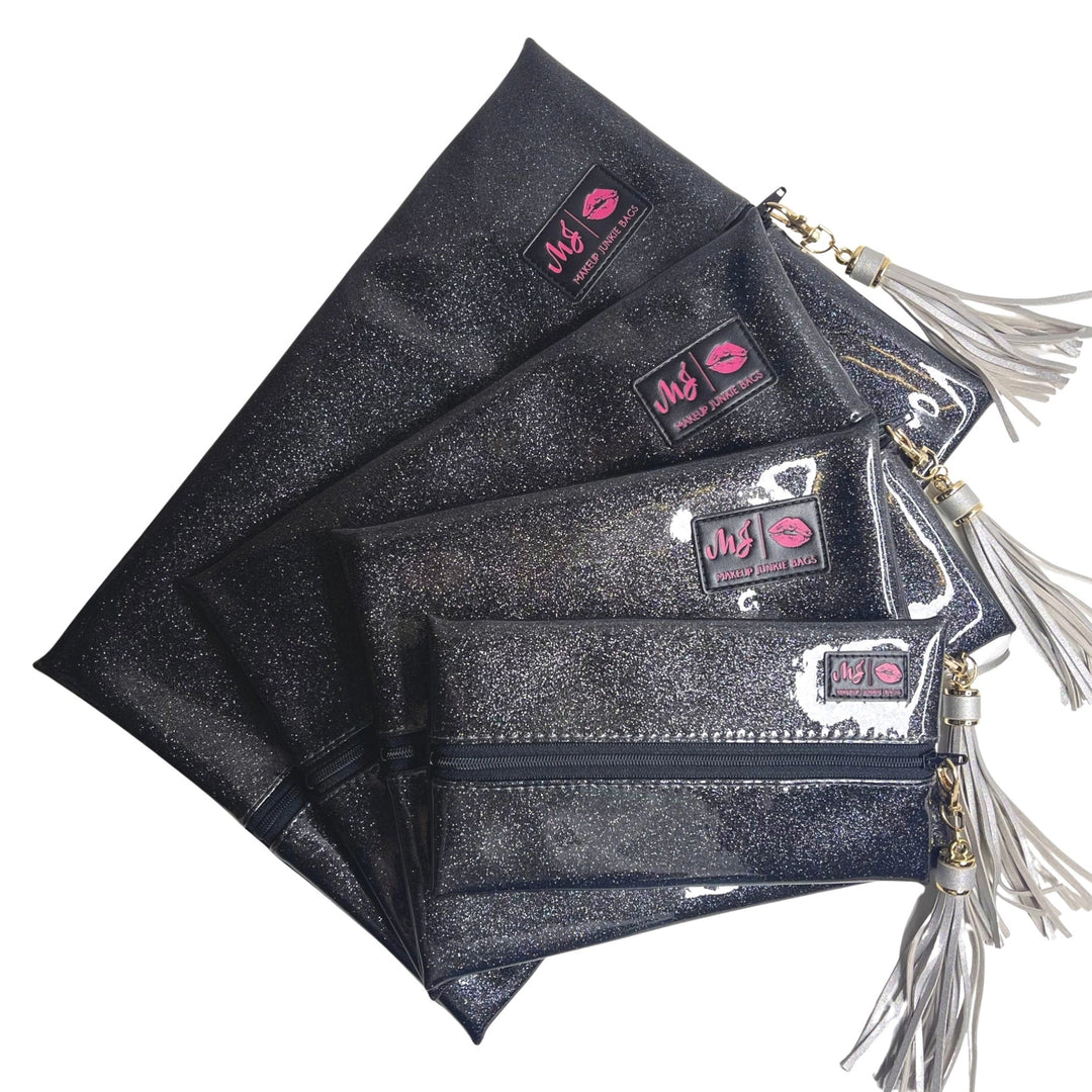 Makeup Junkie Bags grey charcoal stardust glitter clear vinyl zip bags in four sizes fanned out with silver tassel zipper pulls and branded patches, front view on white background