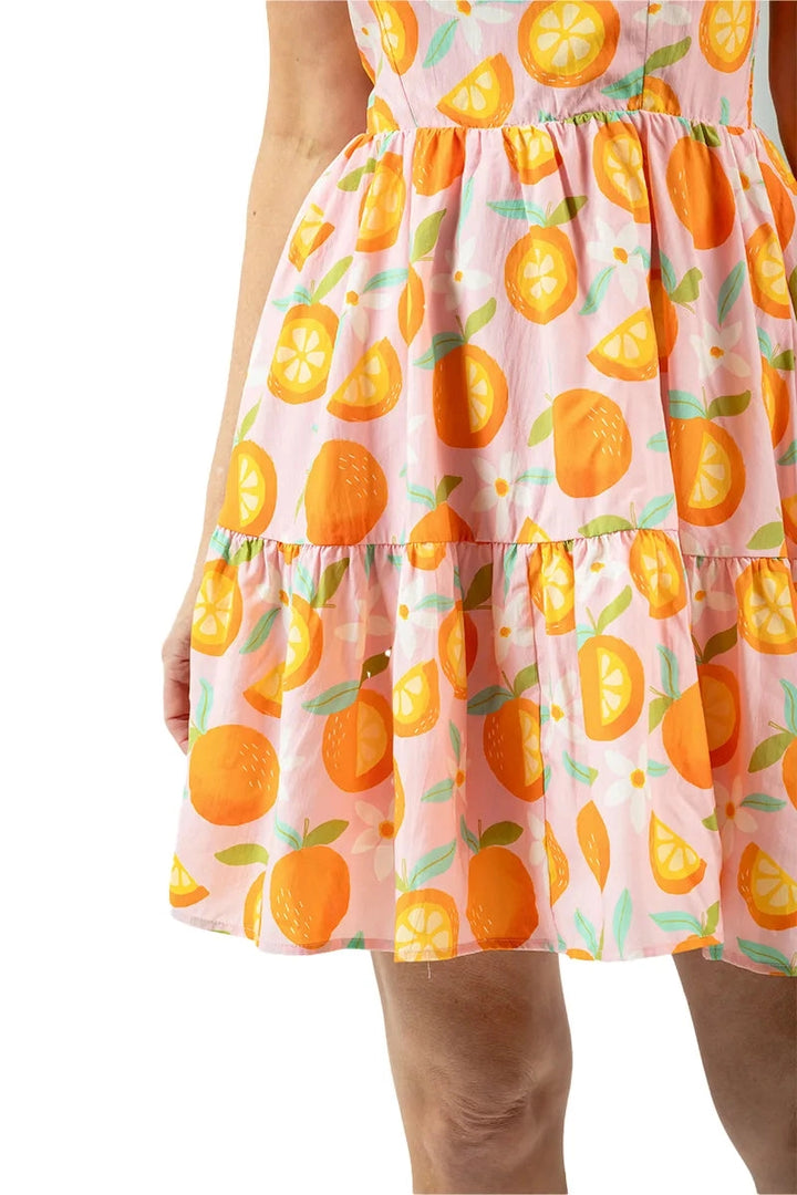 Close-up of two-tier skirt of a pink orange print mini dress showing the gathered tiers and orange fruit print detail.
