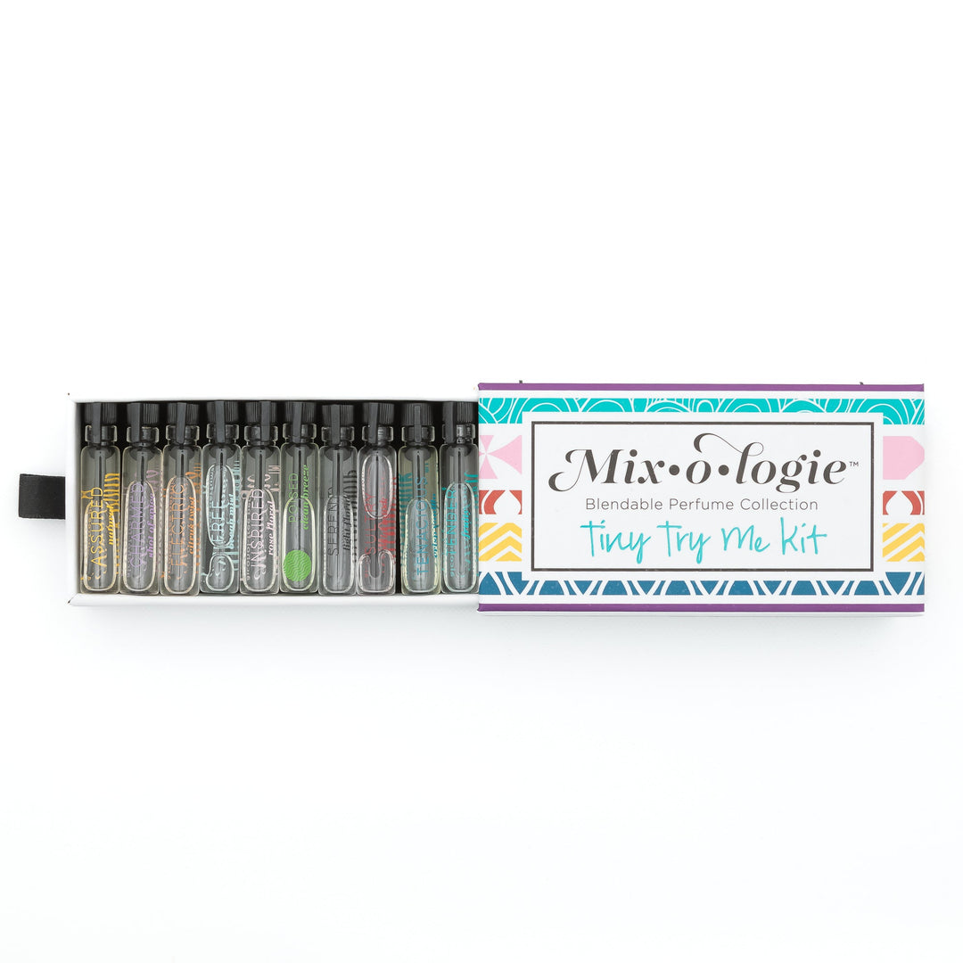 Mixologie Tiny Try Me Kit open slide box on white background showing 12 labeled mini glass perfume vials including Assured, Free, Inspired, and more alongside colorful teal, pink, and yellow patterned box lid