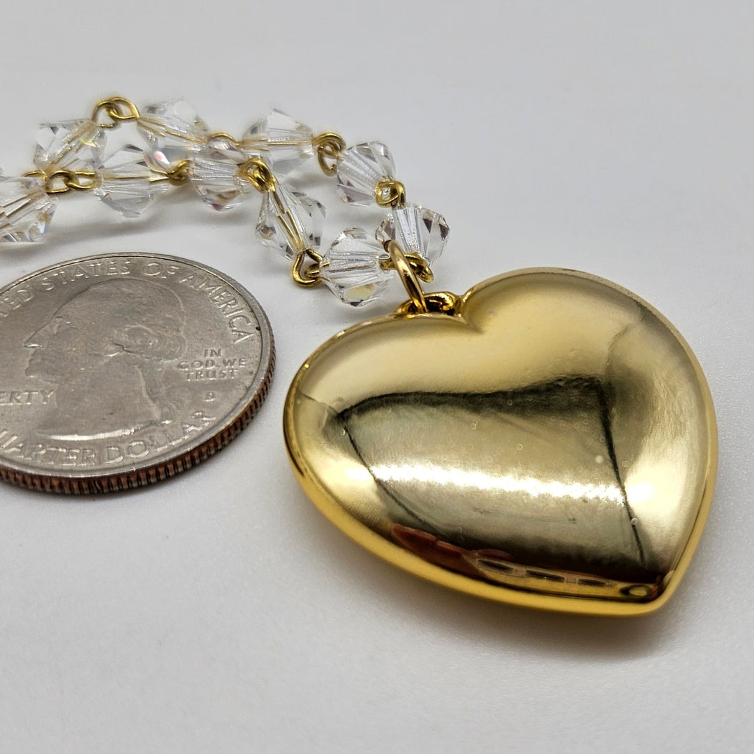 Gold heart-shaped pendant on a chain next to a quarter for scale on a white background