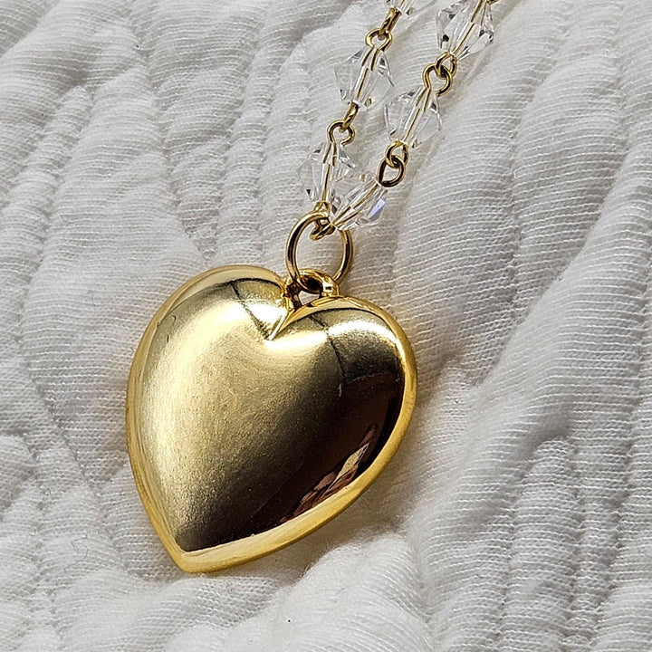 Gold heart-shaped pendant on a chain against a white fabric background