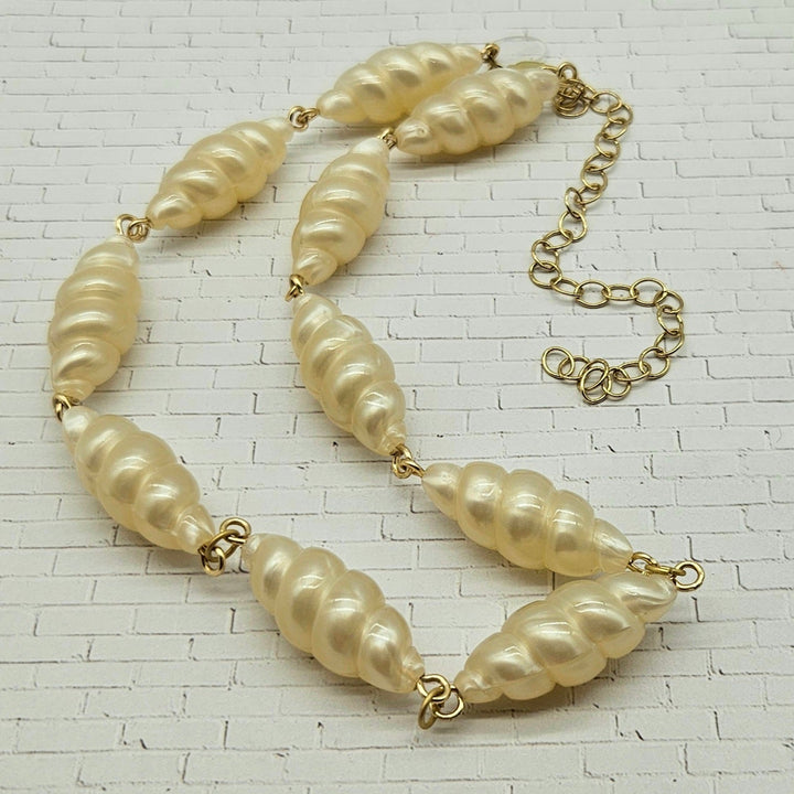 Lucite pearl necklace with gold chain on a textured white background