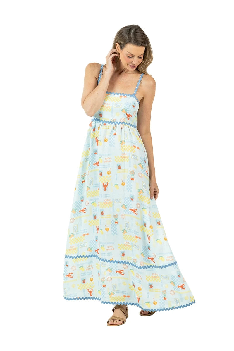 Full-length front view of woman in a light blue lobster and summer print maxi dress with blue ric-rac trim, spaghetti straps, and tan sandals.