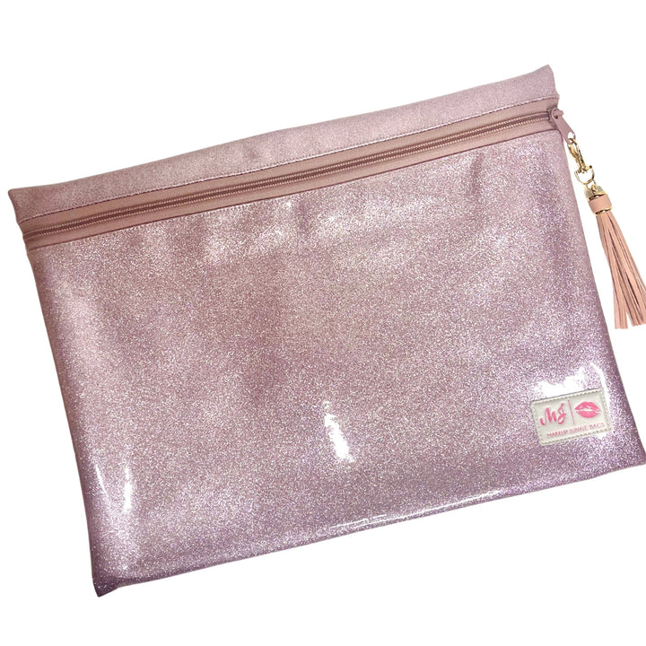 Makeup Junkie Bags blush pink glitter clear vinyl zip makeup bag with blush tassel zipper pull and branded patch, front view on white background