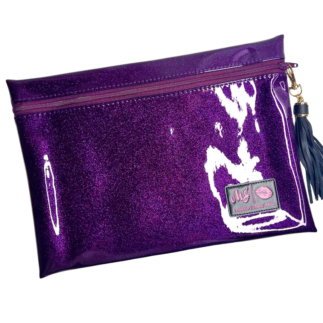 Makeup Junkie Bags deep purple glitter clear vinyl zip makeup bag with navy tassel zipper pull and branded patch, front view on white background