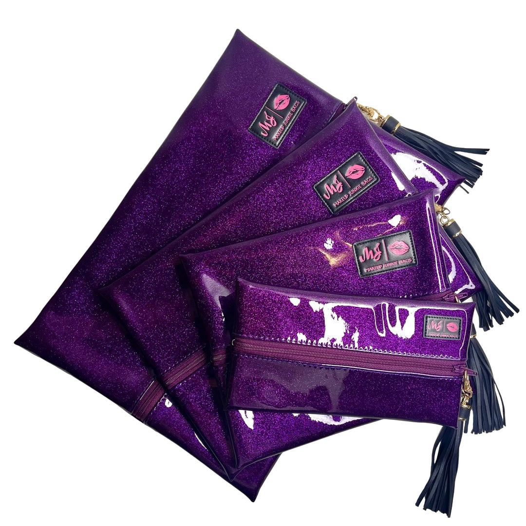 Makeup Junkie Bags deep purple glitter clear vinyl zip bags in four sizes fanned out with navy tassel zipper pulls and branded patches, front view on white background