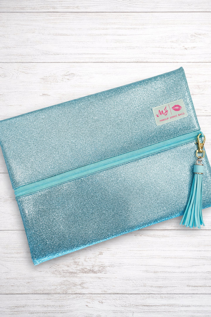 Makeup Junkie Bags mint glitter foldover zip makeup bag closed with mint tassel zipper pull and branded patch, front view on white wood background