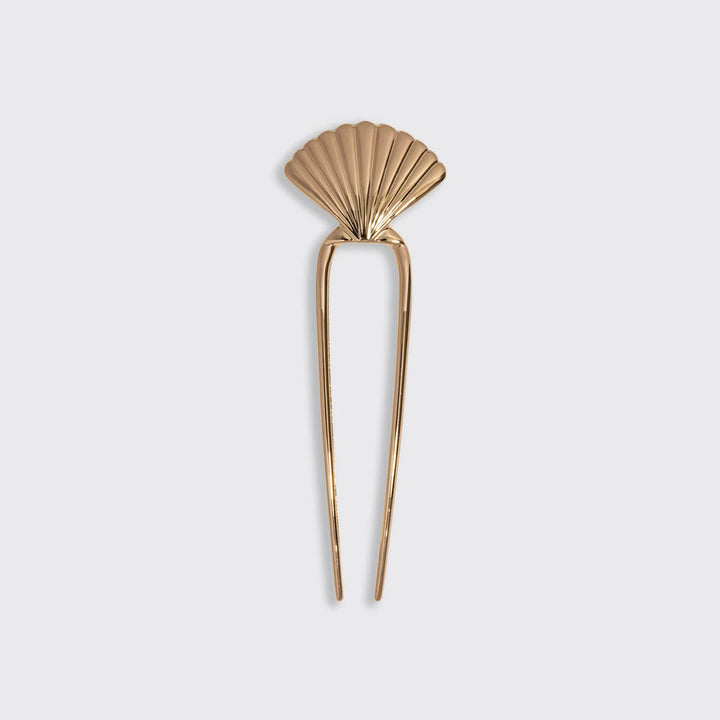Gold scallop shell hair pin with two-prong fork design, on a white background.