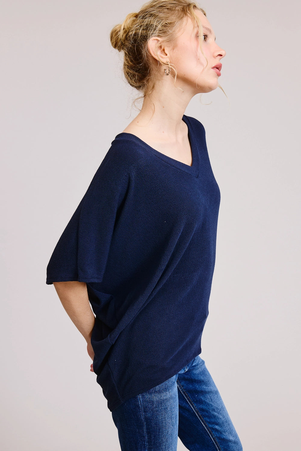 Side view of woman wearing a navy heathered V-neck oversized tee with short dolman sleeves and relaxed boxy fit, styled with dark wash straight-leg jeans.
