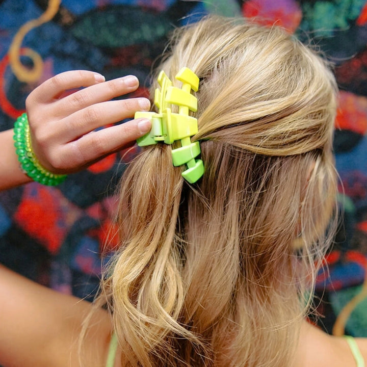 Woman placing Teleties yellow to neon green ombre claw clip into a half-up ponytail hairstyle