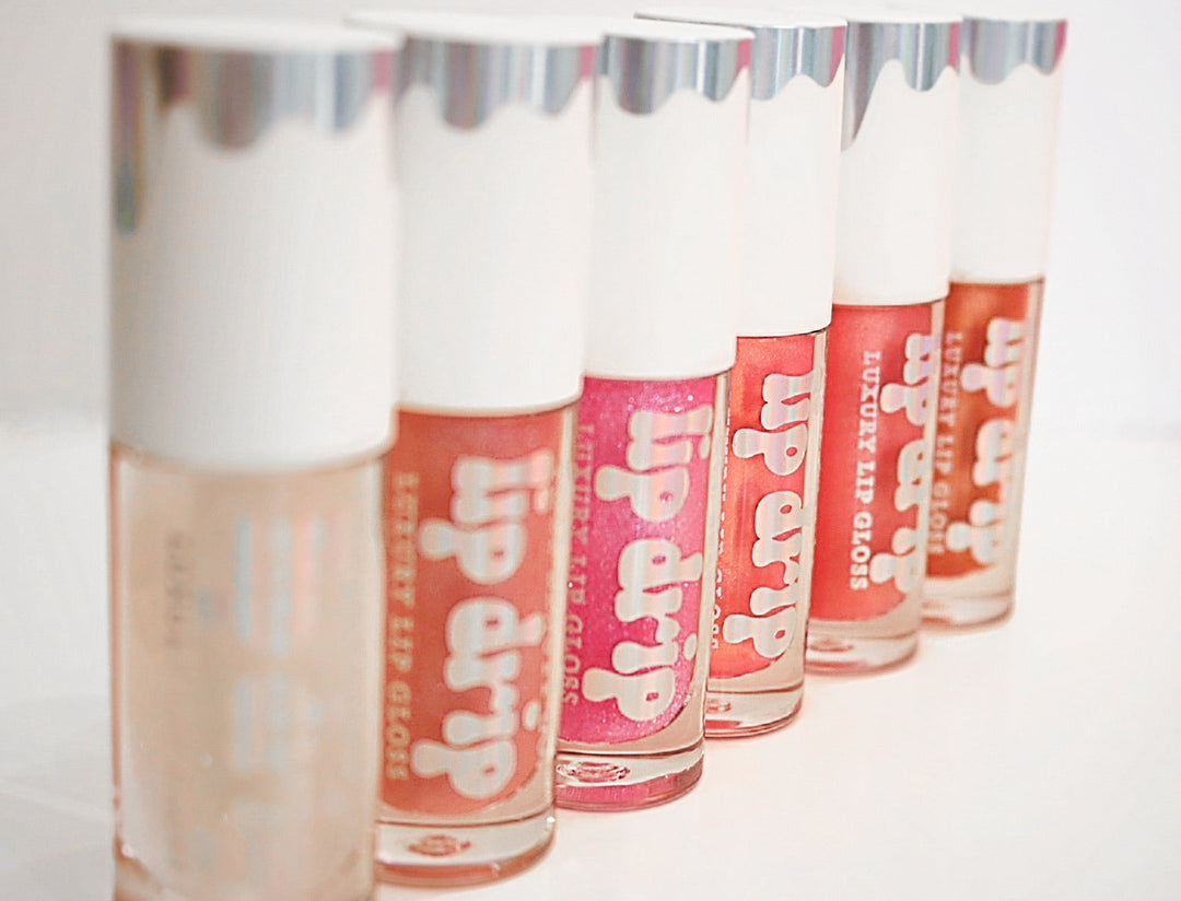 Five Lip Drip Luxury Lip Gloss tubes in nude, coral, pink, and red shades displayed in a row on a white background