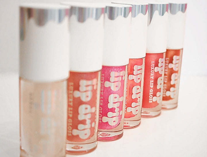 Five Lip Drip Luxury Lip Gloss tubes in nude, coral, pink, and red shades displayed in a row on a white background