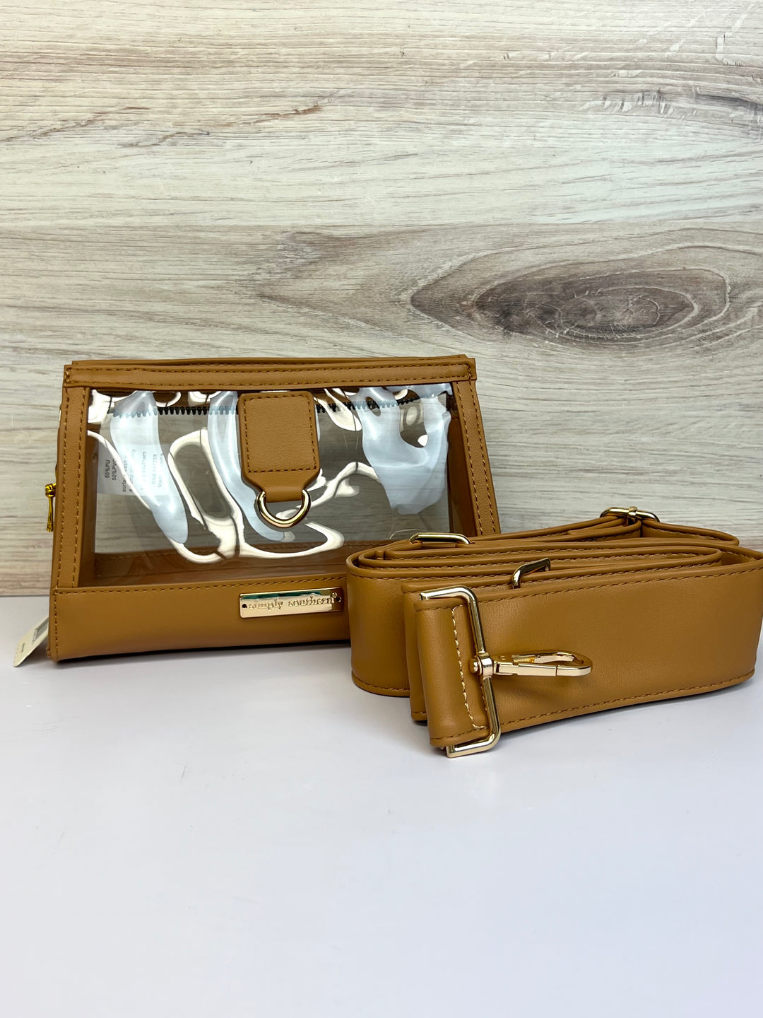 A brown PU leather clutch with a clear accent, alongside a detachable crossbody strap, both displayed on a wooden surface.