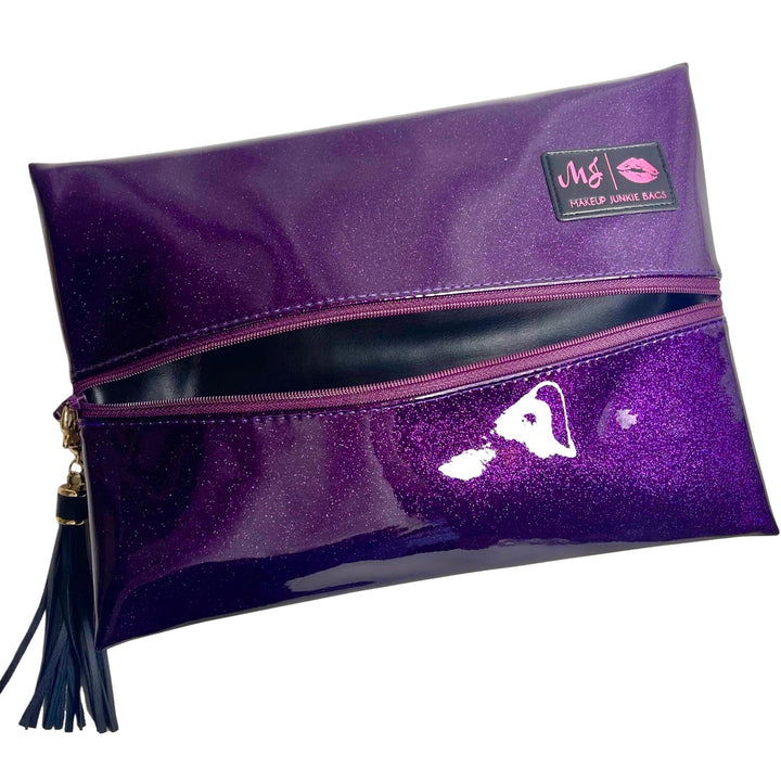 Makeup Junkie Bags deep purple glitter foldover zip makeup bag partially open with navy tassel zipper pull and branded patch, front view on white background