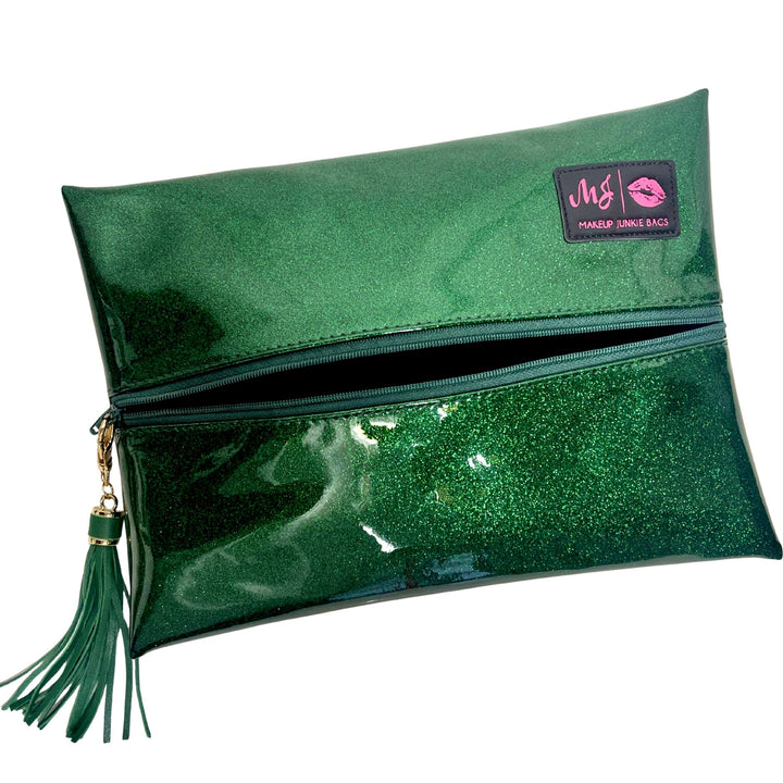 Makeup Junkie Bags emerald green glitter foldover zip makeup bag partially open with green tassel zipper pull and branded patch, front view on white background