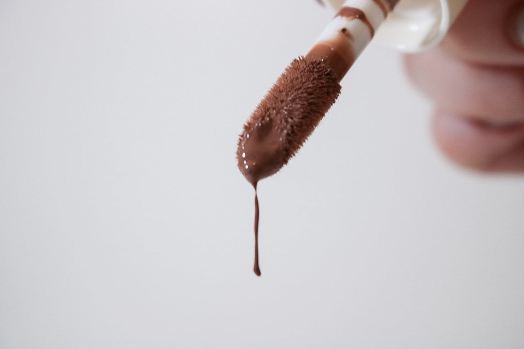 Close-up of Lip Drip Luxury Lip Gloss applicator wand loaded with deep chocolate brown gloss dripping off the tip