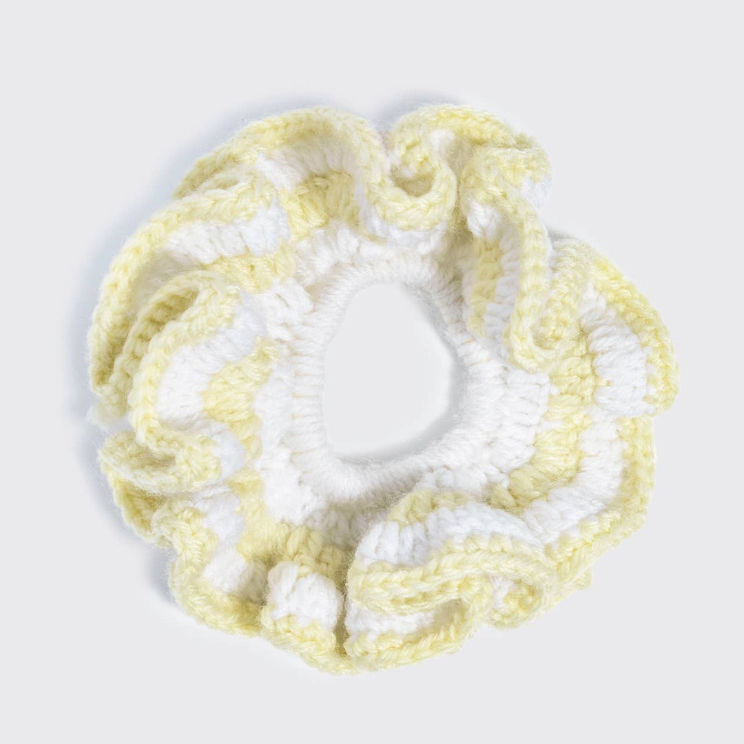 Flat lay top-down view of a butter yellow and white crochet scrunchie with a ruffled, wavy texture, on a white background.