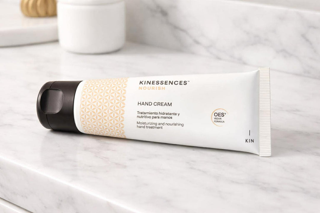 Kinessences Nourish Hand Cream tube with cream and gold geometric label resting on marble surface

