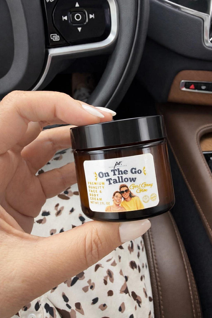 Hand holding an amber glass jar of On The Go Tallow premium face and body cream inside a car interior with leather seats.
