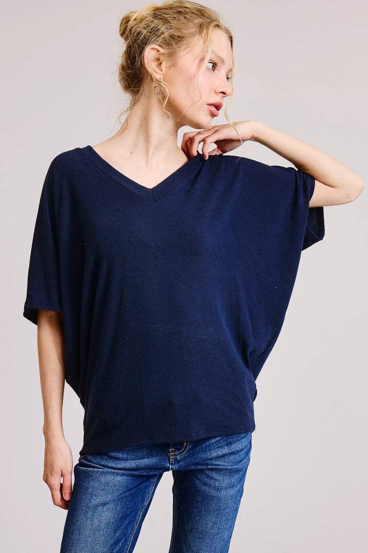 Woman wearing a navy heathered V-neck oversized tee with short dolman sleeves and relaxed boxy fit, styled with dark wash straight-leg jeans and gold hoop earrings.