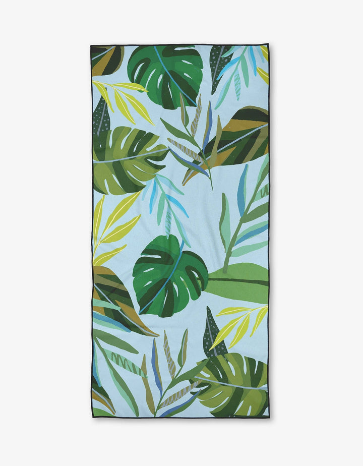 Beach towel featuring a colorful illustrated tropical leaf pattern with monstera and palm leaves on a light blue background