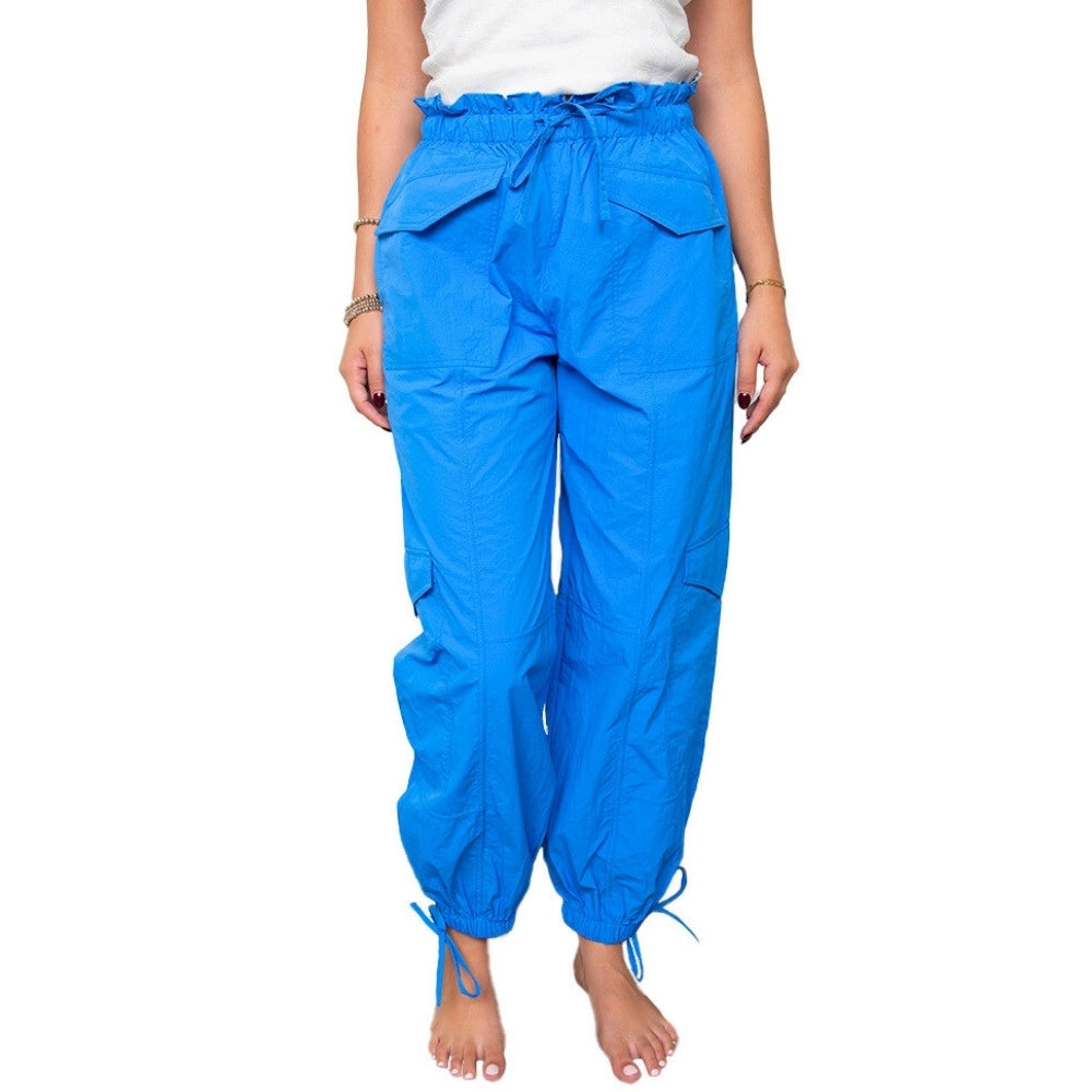 Front view of woman in a white top and cobalt blue paperbag-waist cargo jogger pants with drawstring waist, flap front pockets, side cargo pockets, and tie ankles.