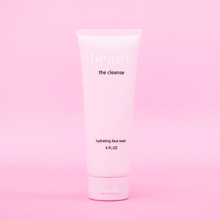 Close-up of a pink squeeze tube dispensing white creamy foam into a clear glass bowl, showing open flip-top cap and hydrating face wash texture.