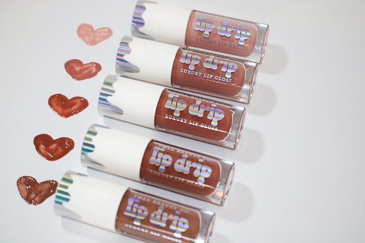 Five Lip Drip Luxury Lip Gloss tubes in nude to deep brown shades displayed with matching heart-shaped color swatches