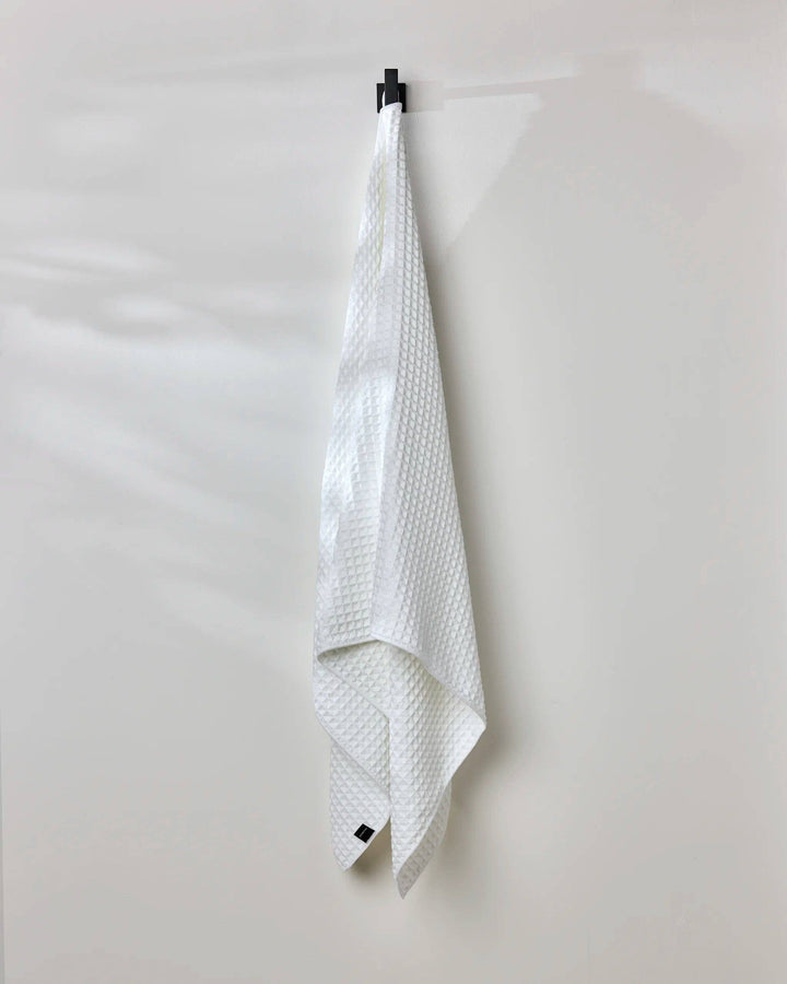 White Cloud Waffle Bath Towel by Geometry hanging on a hook against a wall
