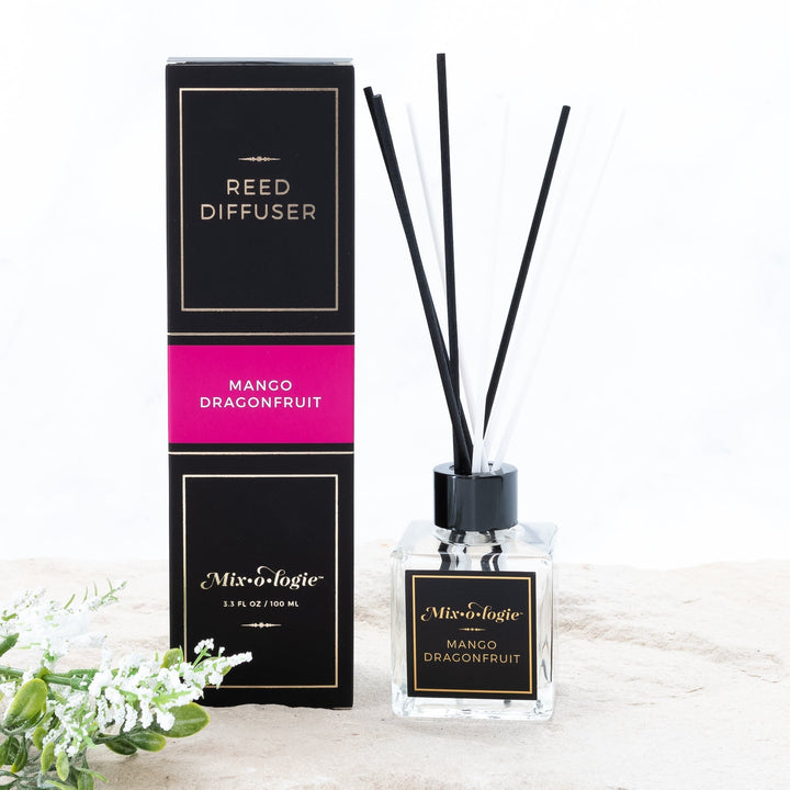 Mixologie Reed Diffuser in Mango Dragonfruit, 3.3 fl oz, clear square glass bottle with black cap and black label with hot pink accent band, with matching black and pink box, styled with white florals