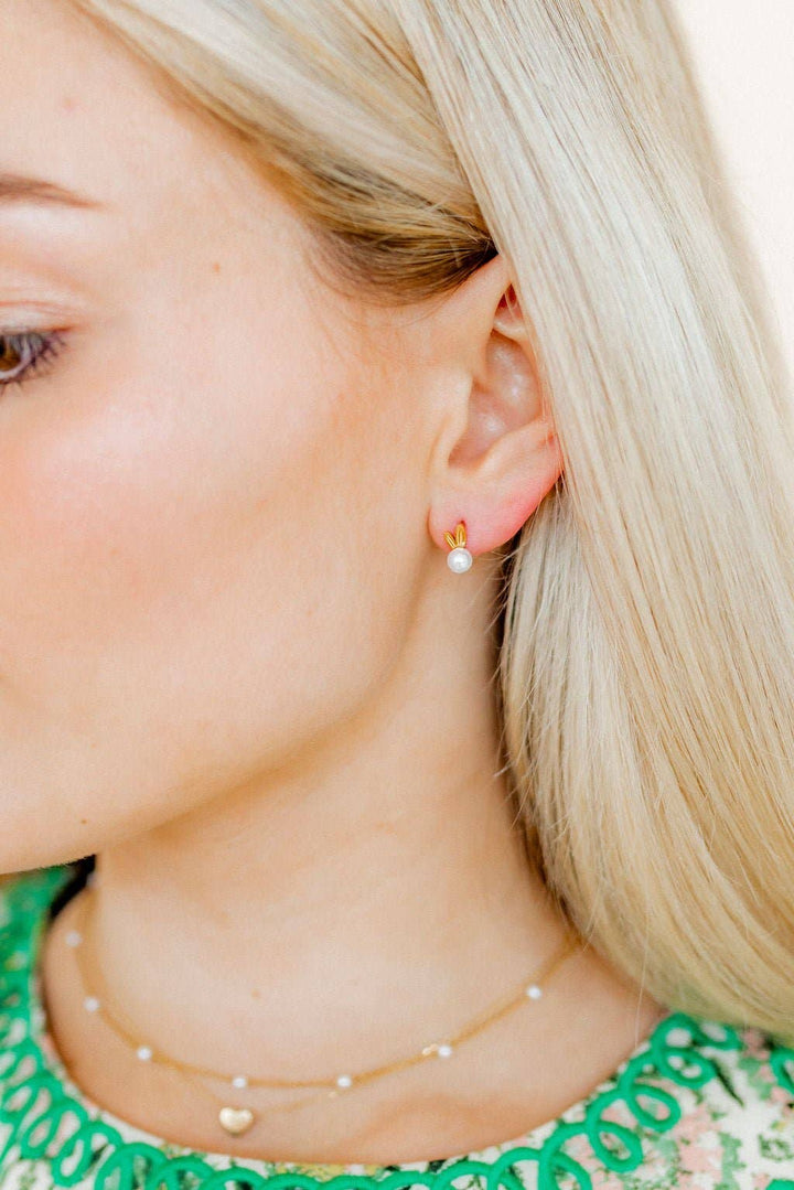 Close-up of gold bunny ear and pearl stud earring worn on ear with blonde hair and a delicate pearl station necklace.