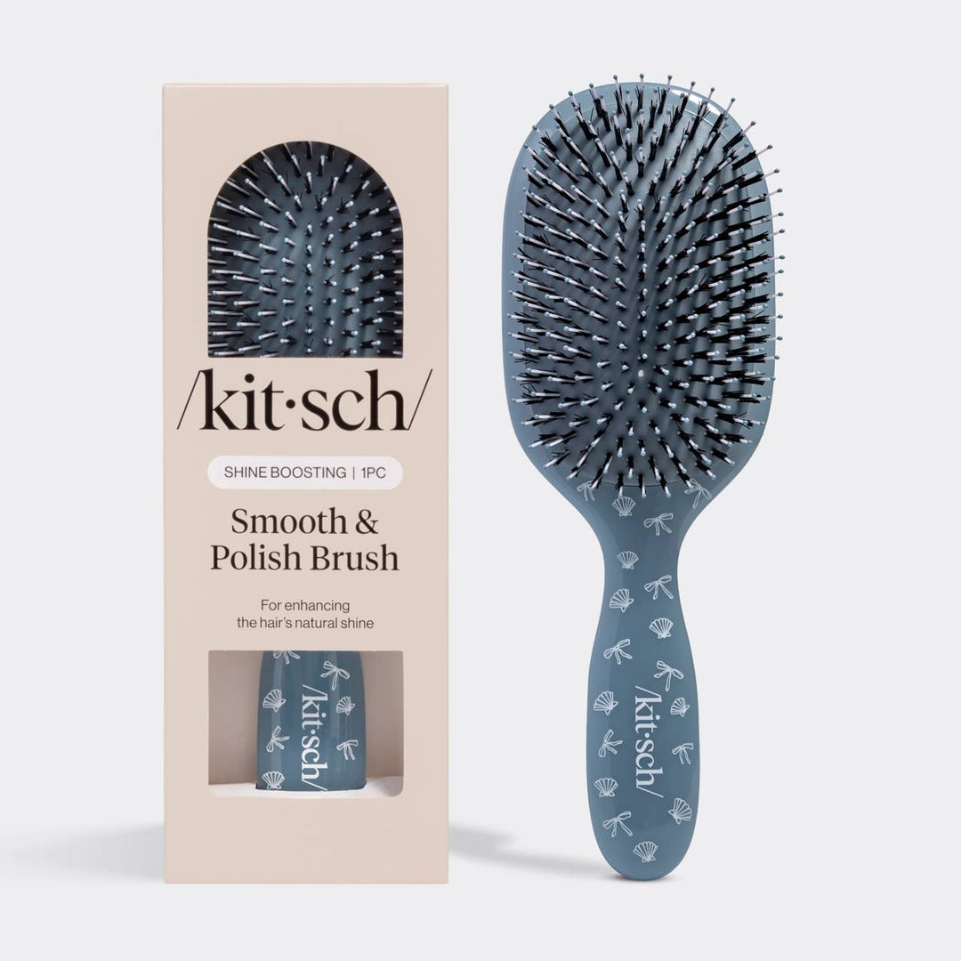 Kitsch Smooth & Polish Brush in slate blue with a seashell and bow print, shown next to its retail packaging box.