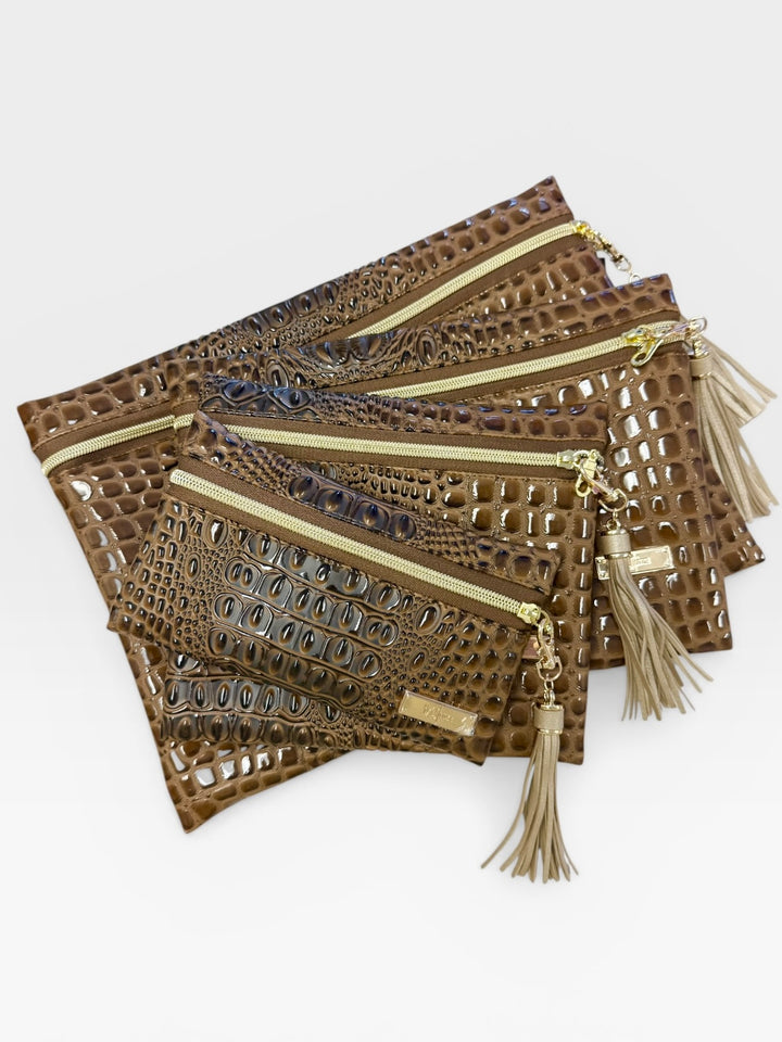 Three-piece olive green crocodile embossed faux leather bag set — large fold-over clutch, medium zip pouch, and small zip pouch — all with gold zippers and tassel pulls, on a white background.