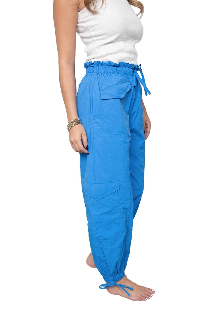 Side view of woman in a white top and cobalt blue paperbag-waist cargo jogger pants showing the flap front pocket, side cargo pocket, and tie ankle detail.