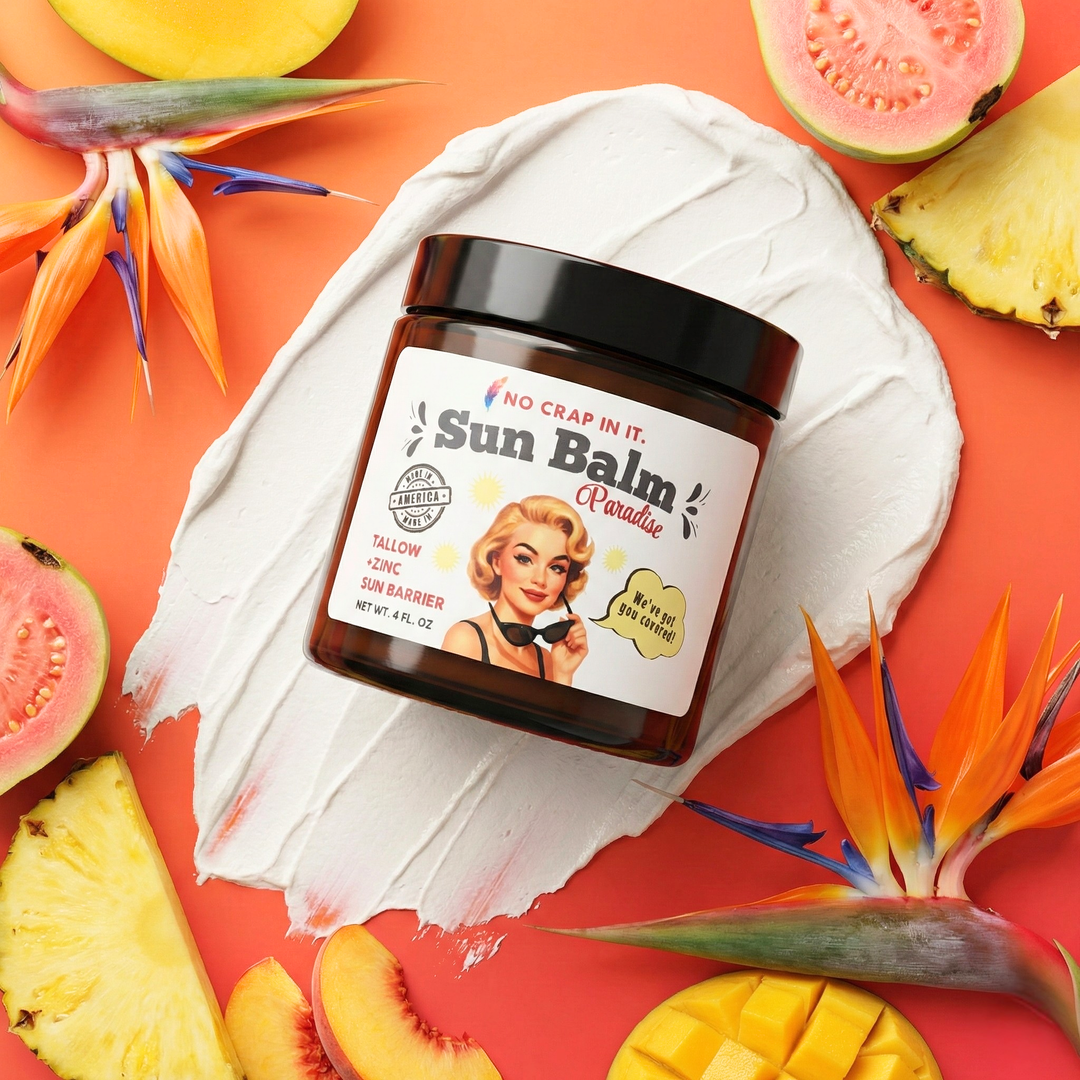 Amber jar with black lid of No Crap In It Sun Balm Paradise Tallow and Zinc Sun Barrier (4 oz) on a white cream smear, surrounded by guava, pineapple, mango, and bird of paradise flowers on a coral orange background.
