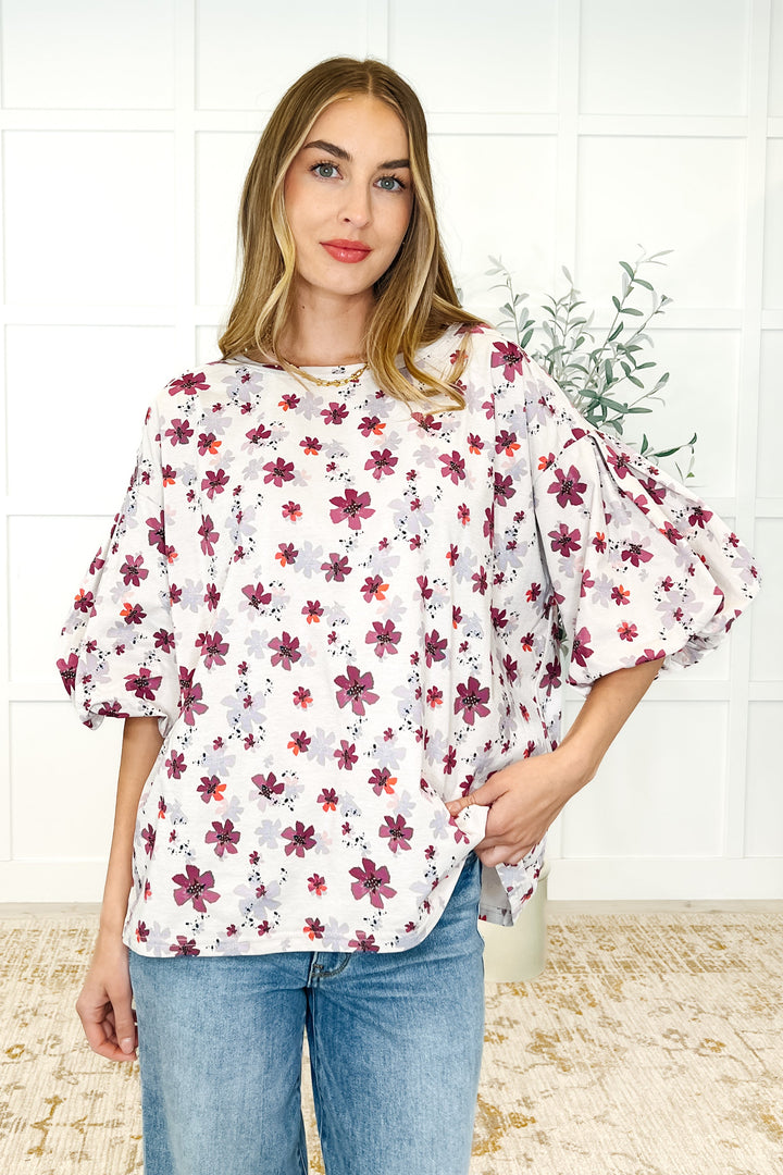 Front view — woman in a white floral puff-sleeve babydoll top with magenta flowers, paired with wide-leg jeans