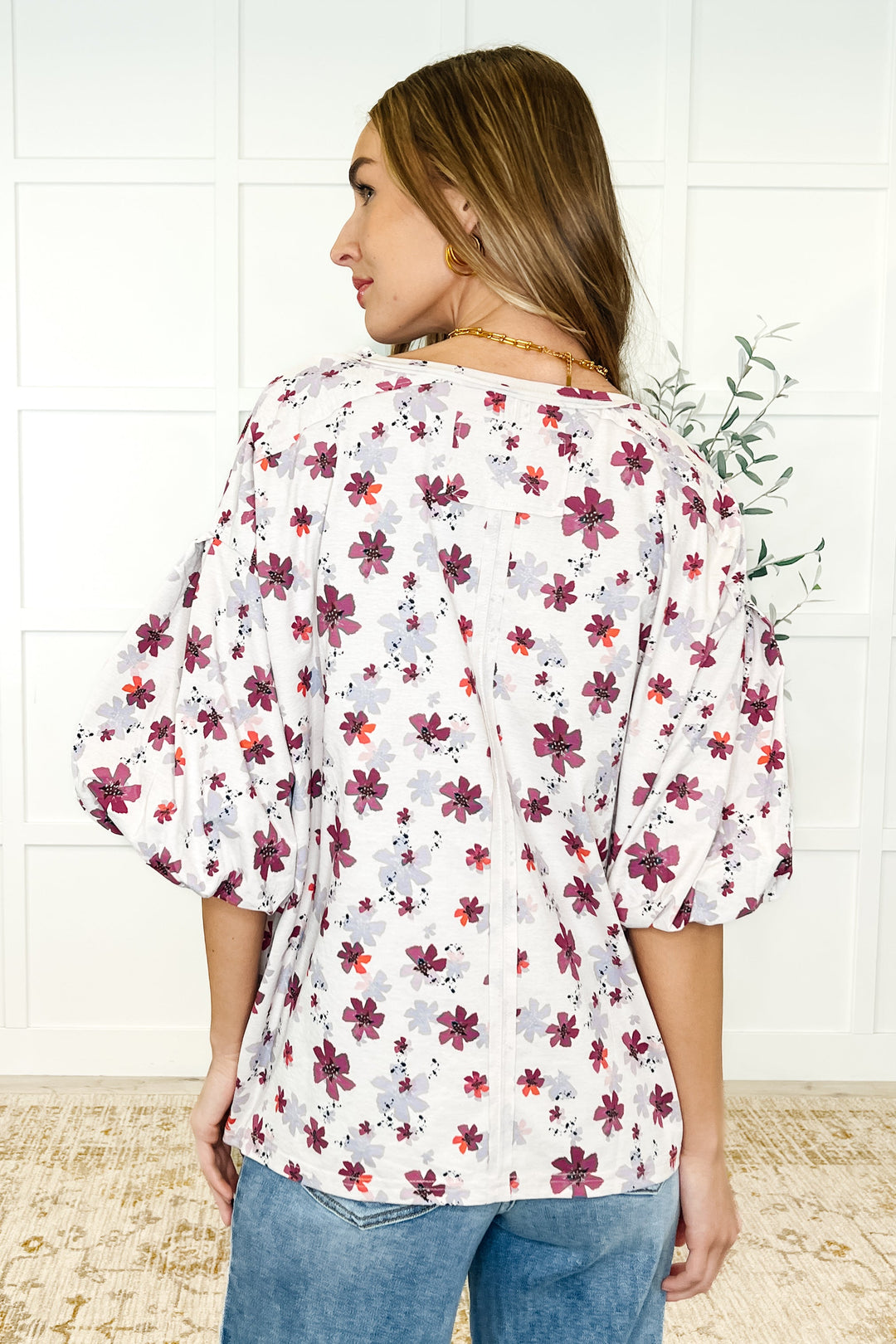 Back view — white floral puff-sleeve babydoll top with magenta flowers, paired with wide-leg jeans