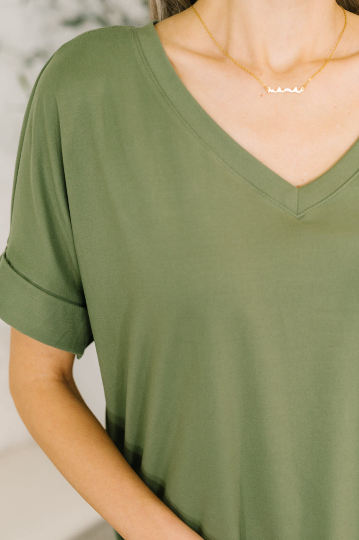 Close-up of the light olive green V-neck neckline with cuffed sleeves and gold necklace