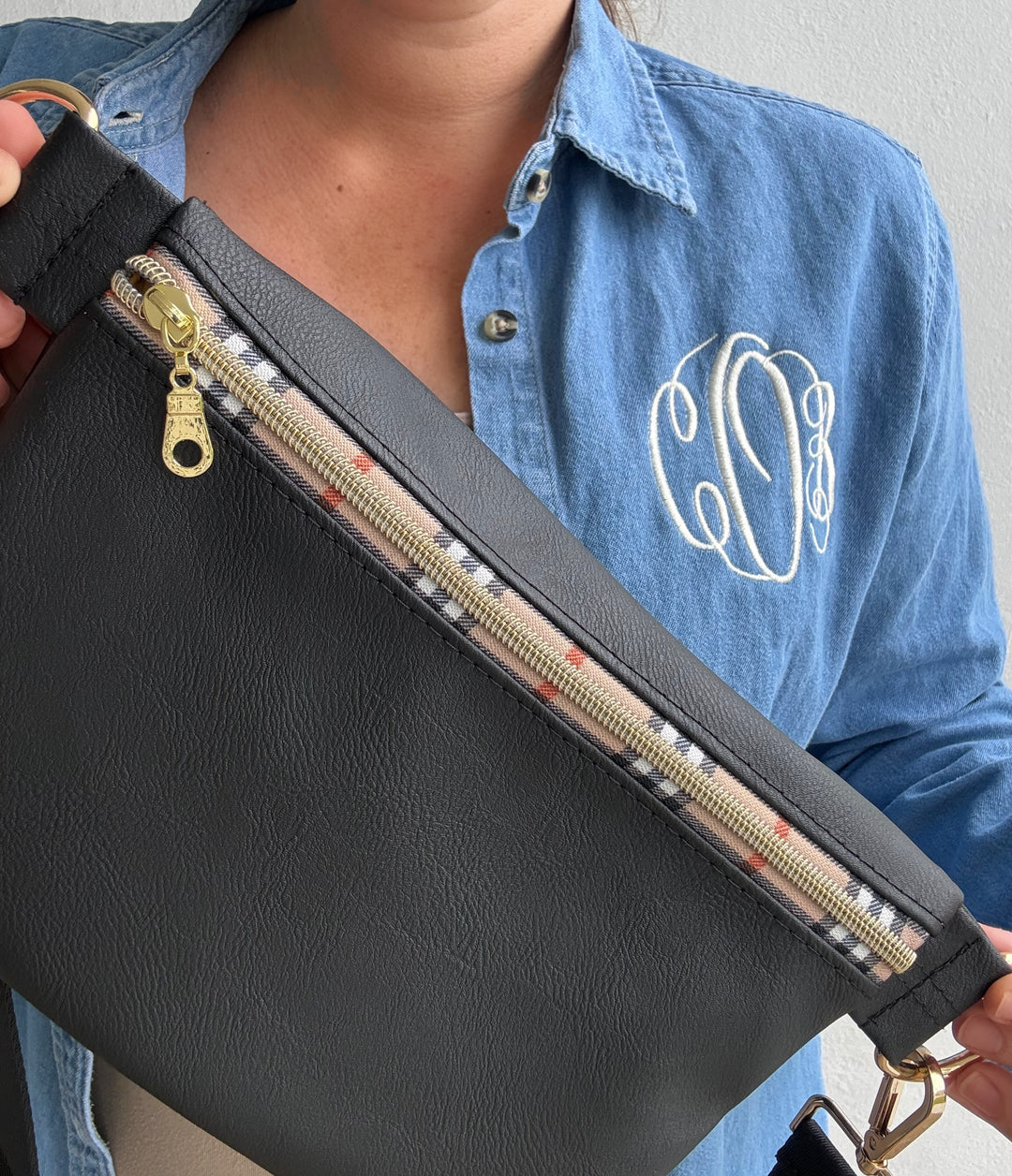 Woman in Prep Obsessed sweatshirt holding large black vegan leather Makeup Junkie zip pouch with plaid-trim gold zipper and tassel