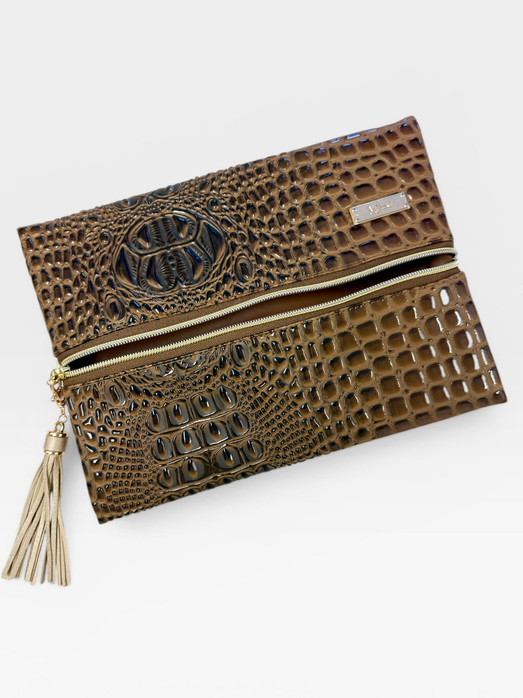 Olive green crocodile embossed faux leather fold-over clutch with gold zipper, tassel pull, and embossed monogram medallion detail on the flap, on a white background.