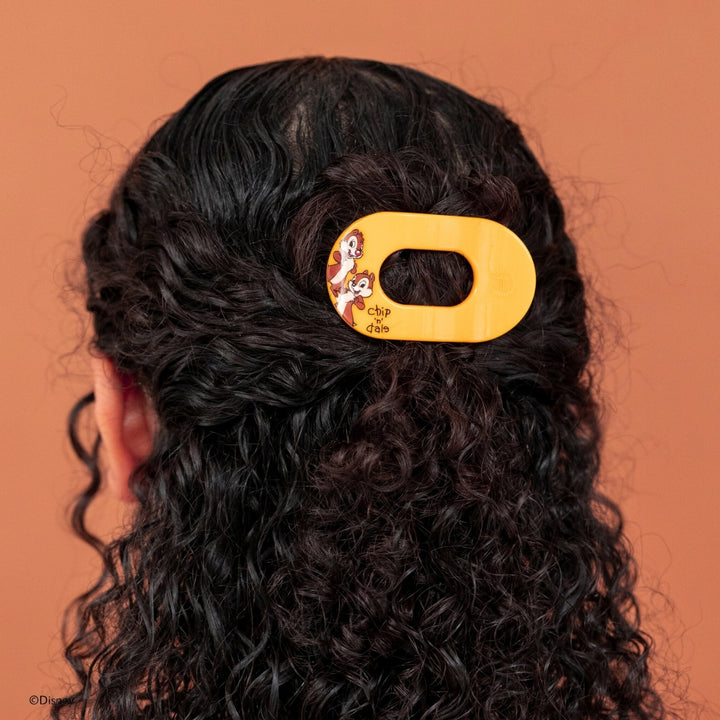 Disney x Teleties Chip 'n Dale tiny flat round hair clip in amber yellow securing a half-up style on curly black hair against terracotta background