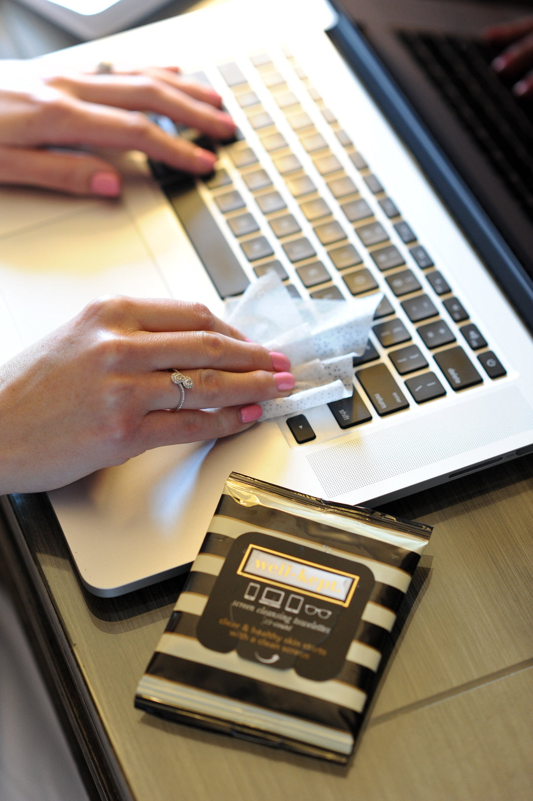 Someone cleans a laptop keyboard using BUCKHEAD electronics cleaning wipes, with a packet of BUCKHEAD wipes placed nearby.