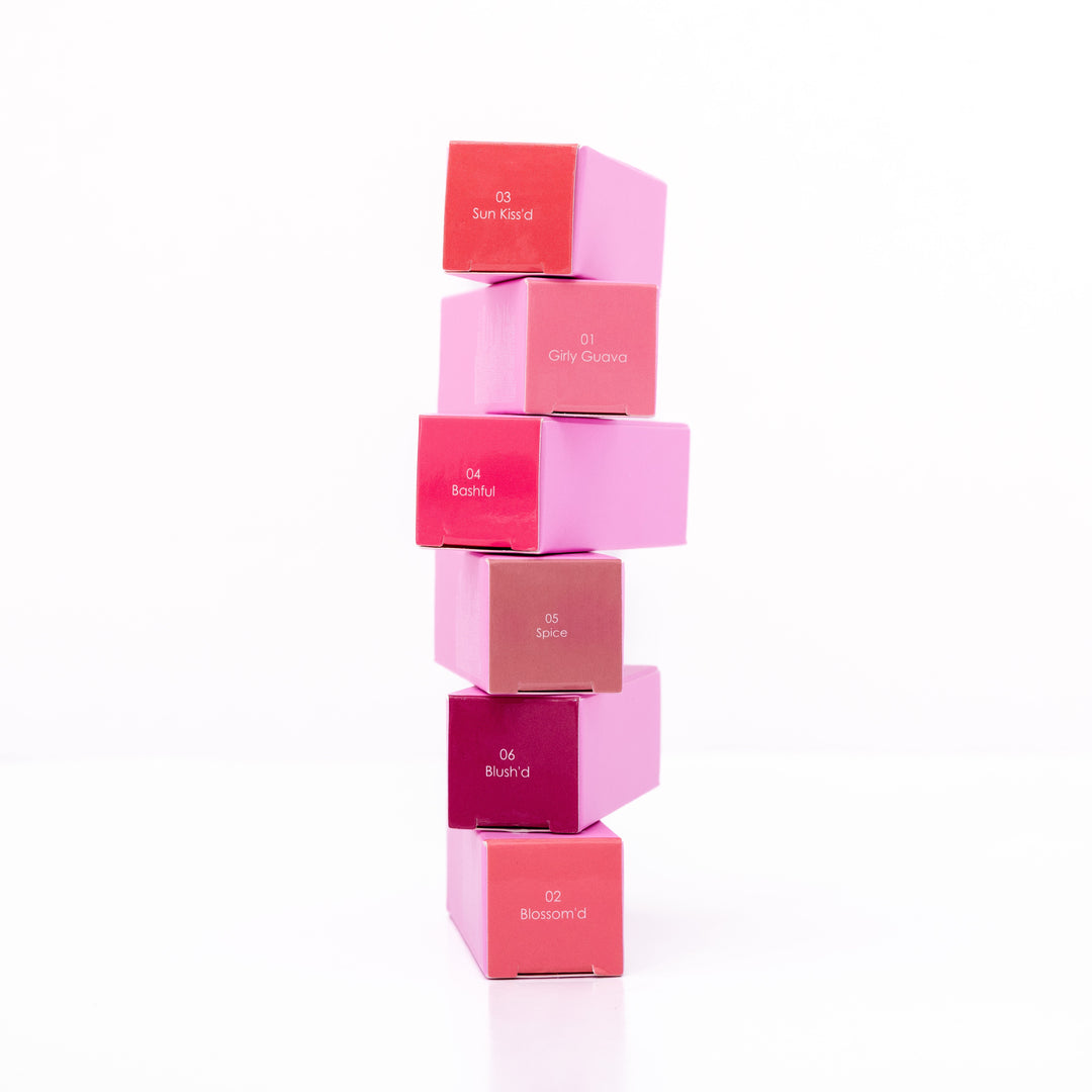 Beaut. Lip Gloss'd six color-matched square boxes stacked vertically showing shades 03 Sun Kiss'd, 01 Girly Guava, 04 Bashful, 05 Spice, 06 Blush'd, and 02 Blossom'd on white background