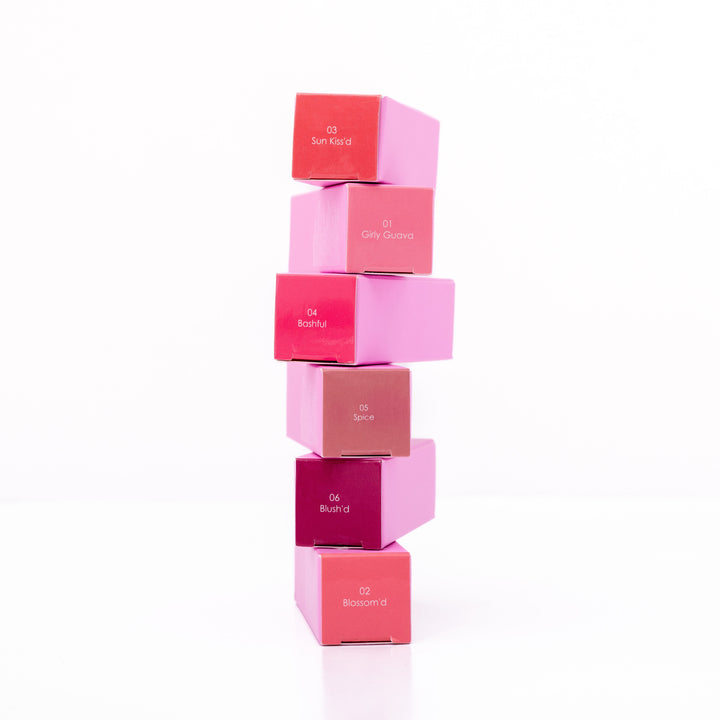 Beaut. Lip Gloss'd six color-matched square boxes stacked vertically showing shades 03 Sun Kiss'd, 01 Girly Guava, 04 Bashful, 05 Spice, 06 Blush'd, and 02 Blossom'd on white background